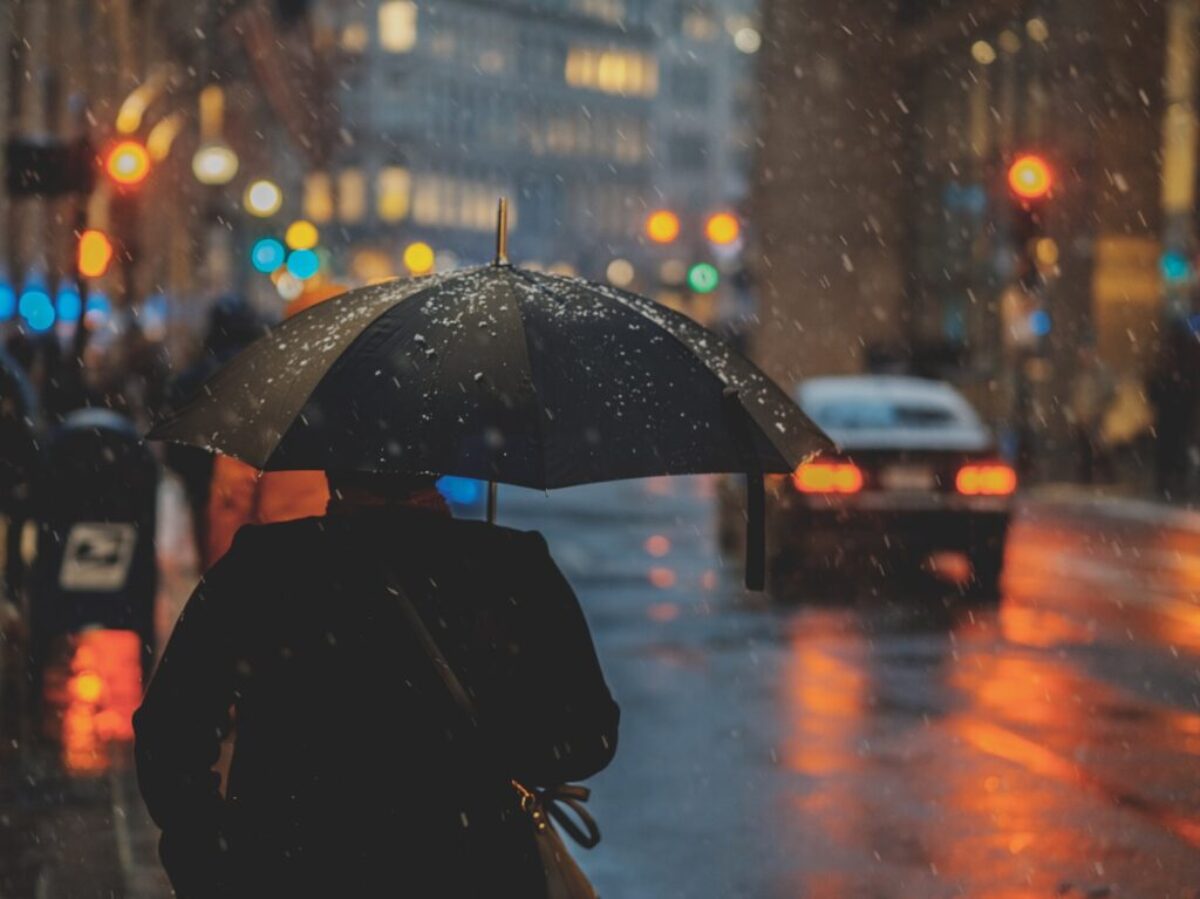 person walking on street and holding umbrella while raining with vehicle nearby