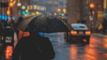 person walking on street and holding umbrella while raining with vehicle nearby