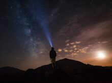 man standing at mountain peak under starry night sky
