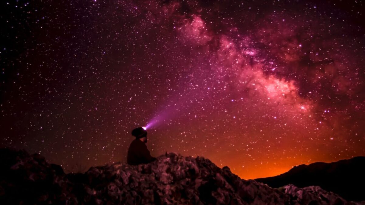 silhouette photo of person holding flashlight under milk way