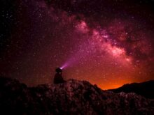 silhouette photo of person holding flashlight under milk way