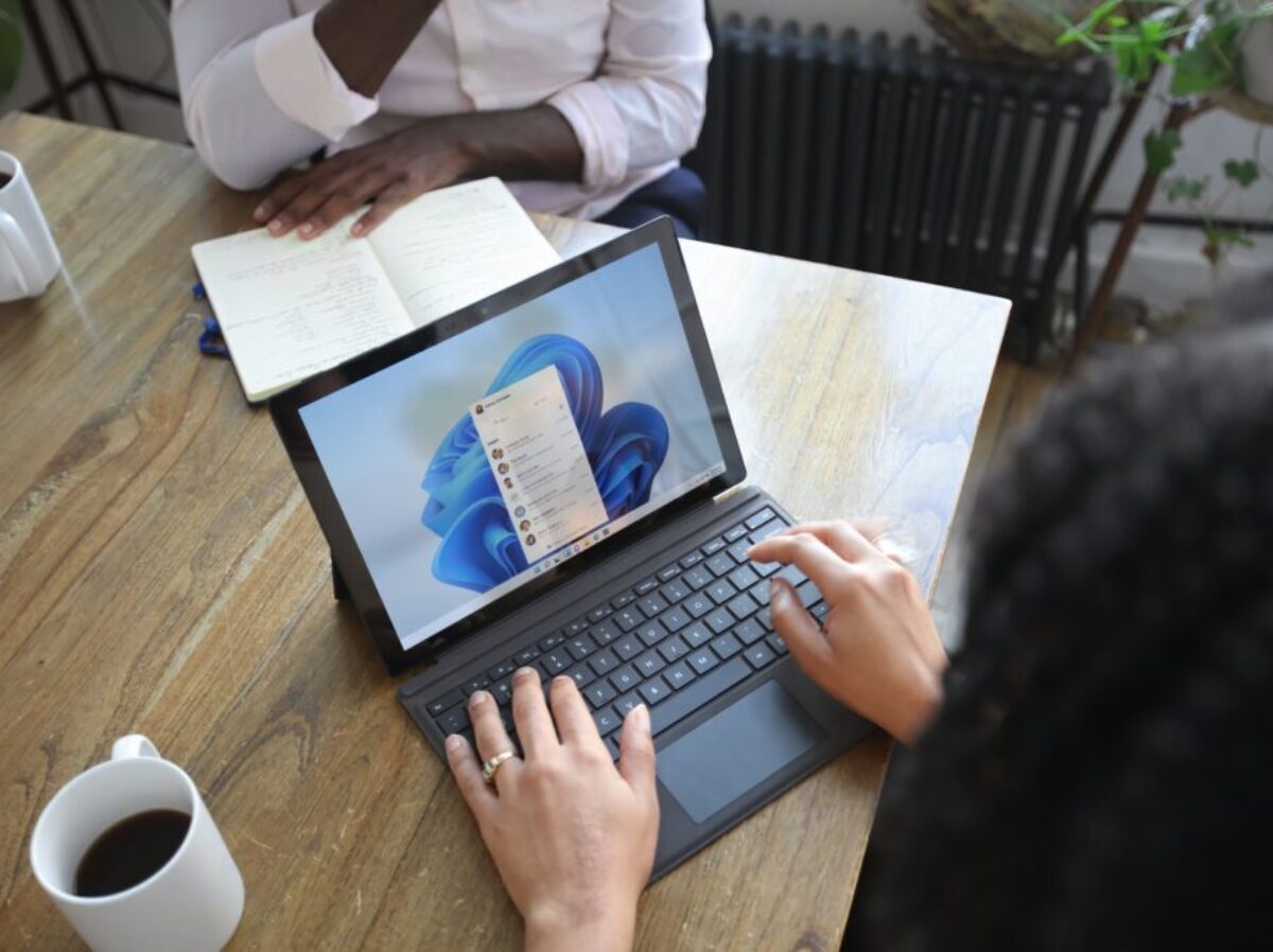 Overhead view of two people at a table working with a Microsoft laptop and notebook