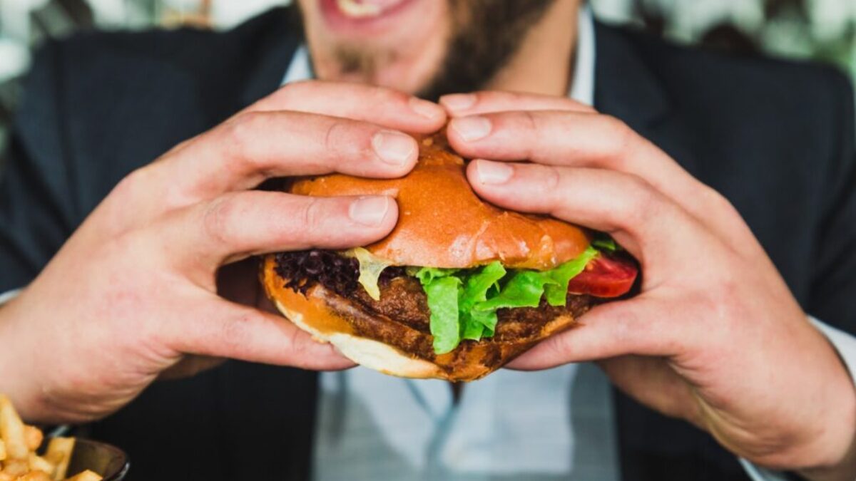 person holding burger bun with vegetables and meat