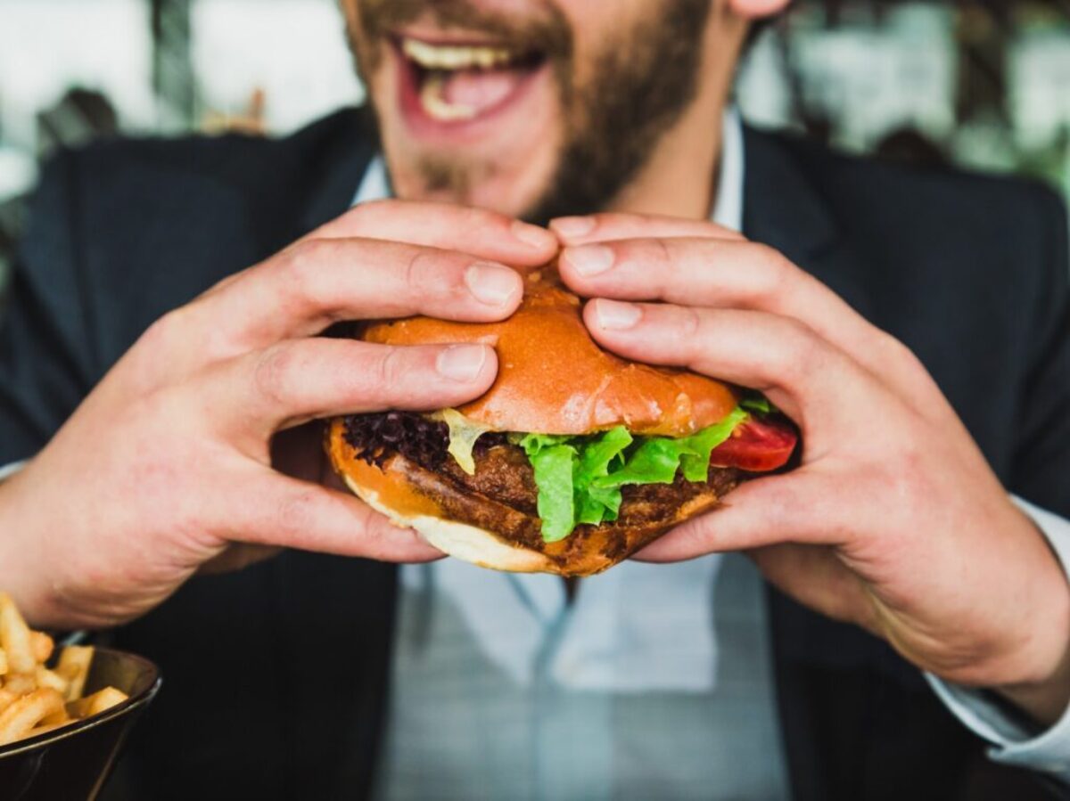 person holding burger bun with vegetables and meat