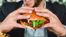 person holding burger bun with vegetables and meat