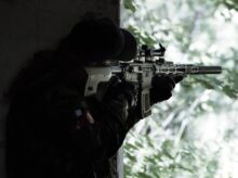 man in black jacket holding black rifle