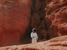photography of astronaut standing beside rock formation during daytime