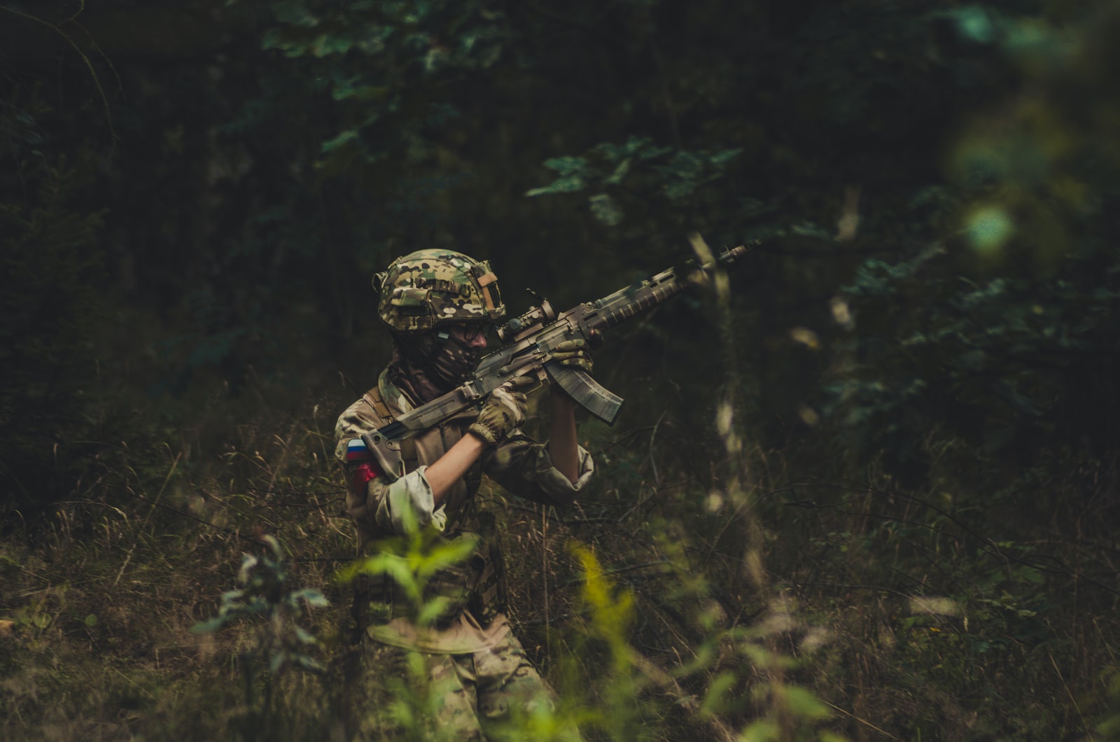 man pointing assault rifle near trees