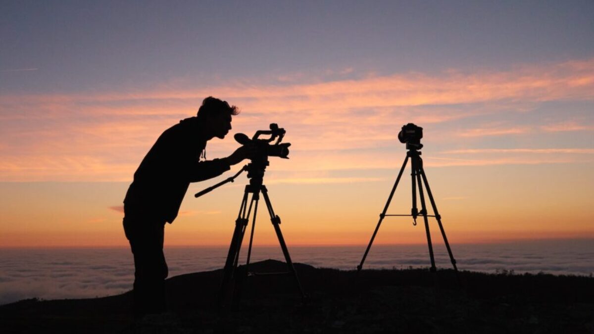 silhouette photo of person holding camera on tripod stand outside
