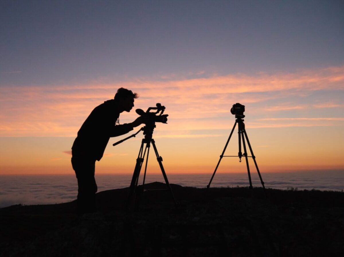 silhouette photo of person holding camera on tripod stand outside