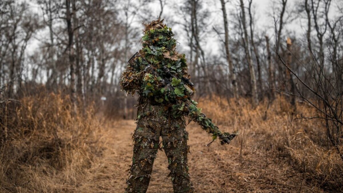 man in green and black camouflage jacket standing on brown grass field during daytime