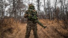 man in green and black camouflage jacket standing on brown grass field during daytime