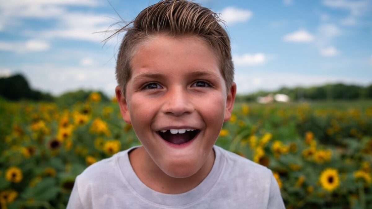boy in white crew neck shirt standing on yellow flower field during daytime