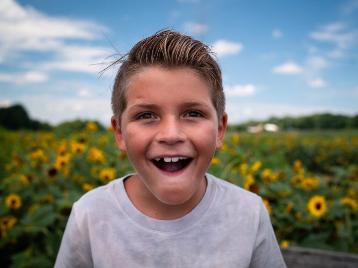 boy in white crew neck shirt standing on yellow flower field during daytime