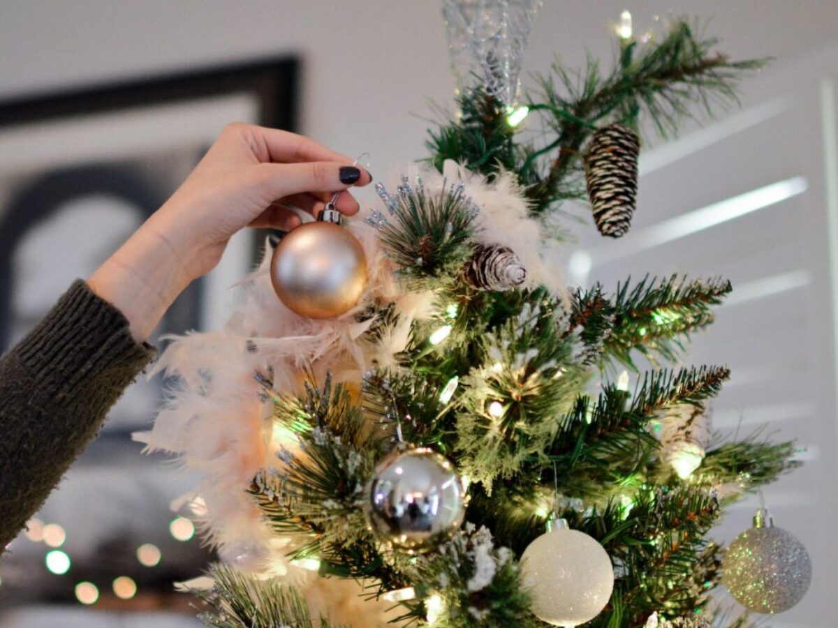 Person Holding Beige Bauble Near Christmas Tree