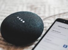 turned-on charcoal Google Home Mini and smartphone