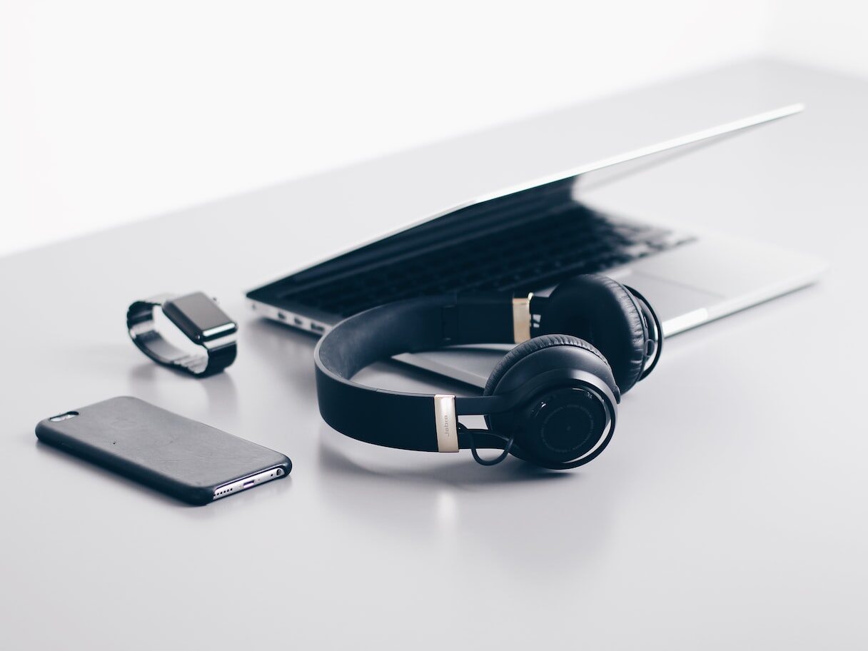 black cordless headphones beside closed black laptop computer and smartphone