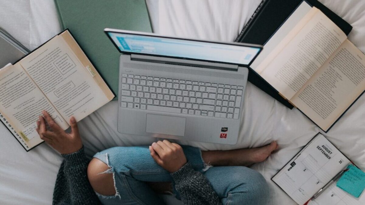woman in blue long sleeve shirt and blue denim jeans sitting on bed using laptop