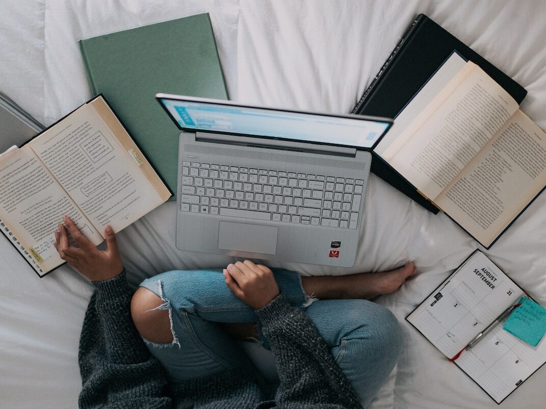 woman in blue long sleeve shirt and blue denim jeans sitting on bed using laptop