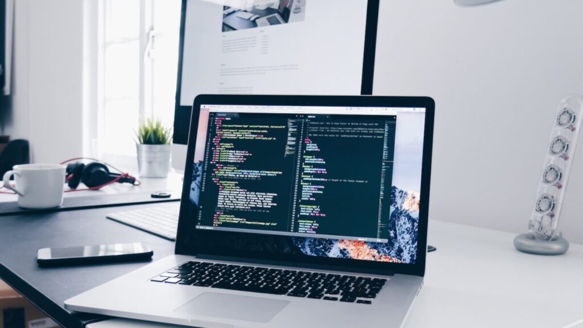 A MacBook with lines of code on its screen on a busy desk