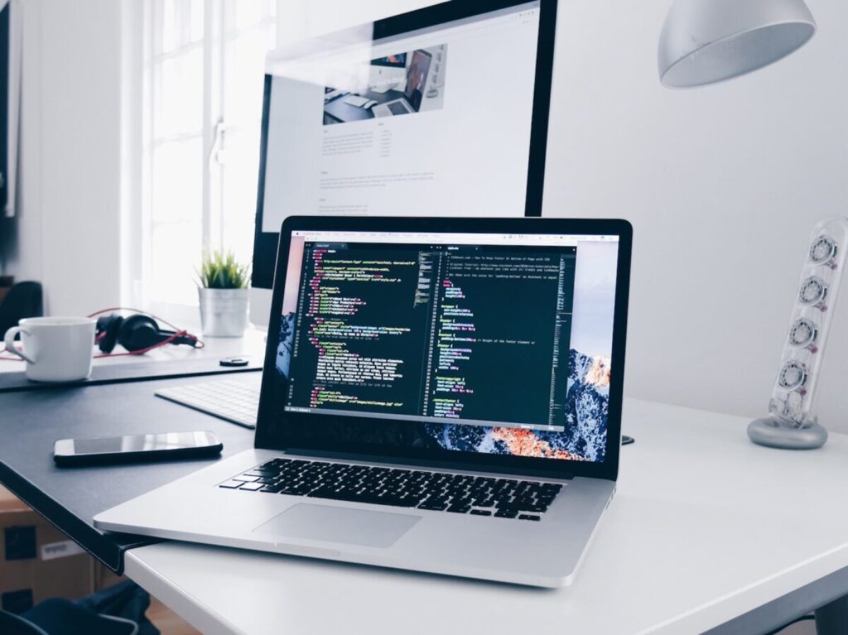 A MacBook with lines of code on its screen on a busy desk