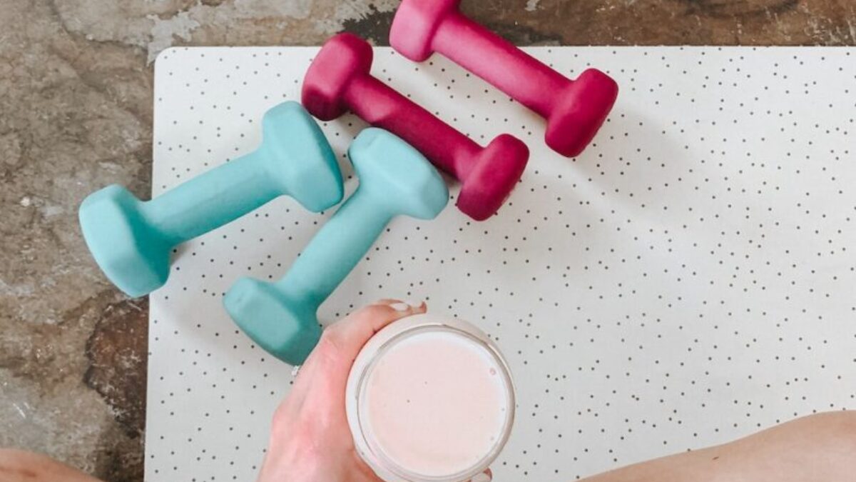 person holding white liquid filled cup above two pairs of dumbbells