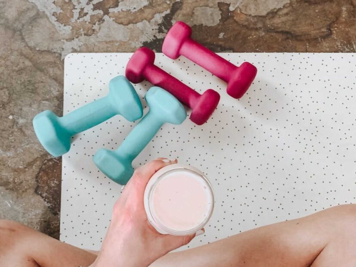 person holding white liquid filled cup above two pairs of dumbbells