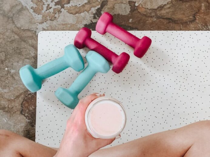 person holding white liquid filled cup above two pairs of dumbbells