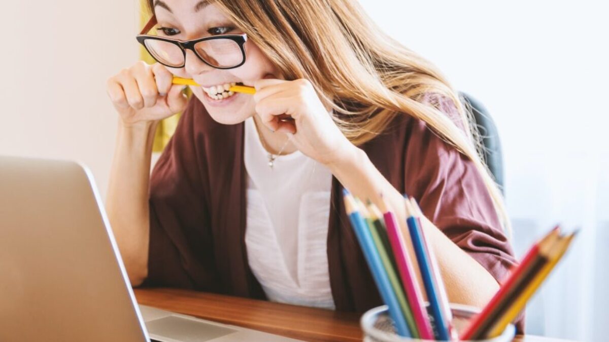 woman biting pencil while sitting on chair in front of computer during daytime