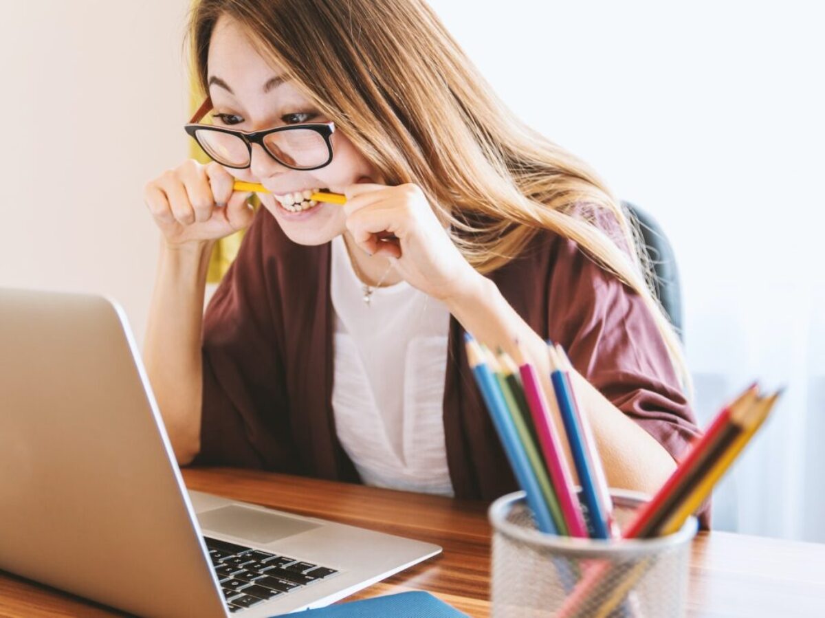 woman biting pencil while sitting on chair in front of computer during daytime