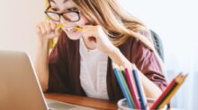 woman biting pencil while sitting on chair in front of computer during daytime