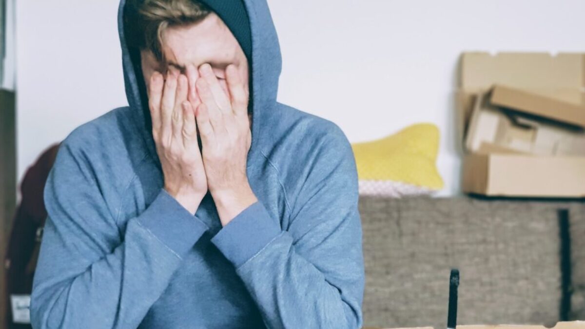 man covering face with both hands while sitting on bench