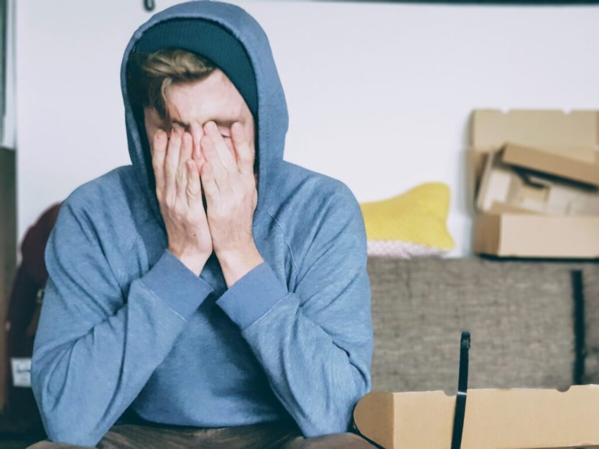 man covering face with both hands while sitting on bench
