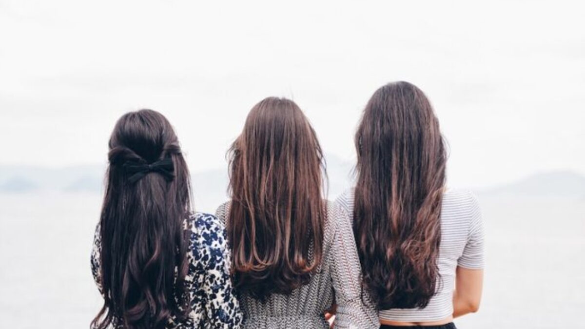 three woman looking back and facing body of water