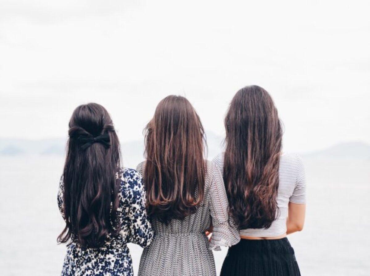 three woman looking back and facing body of water
