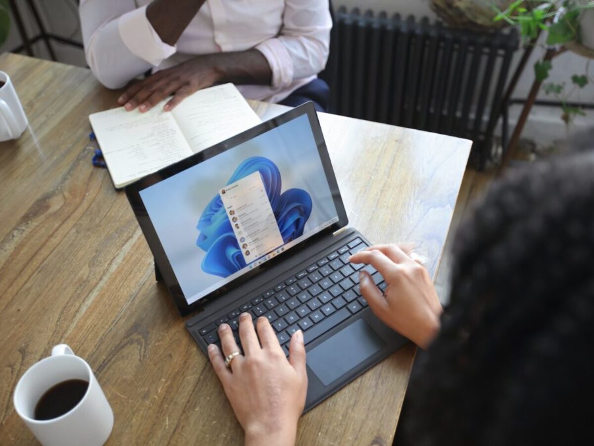 Overhead view of two people at a table working with a Microsoft laptop and notebook