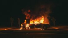 burning grey sedan near trees and signboard at night
