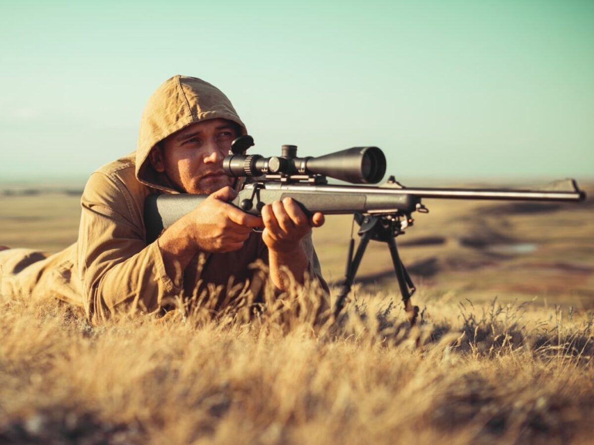 man in brown jacket holding black rifle