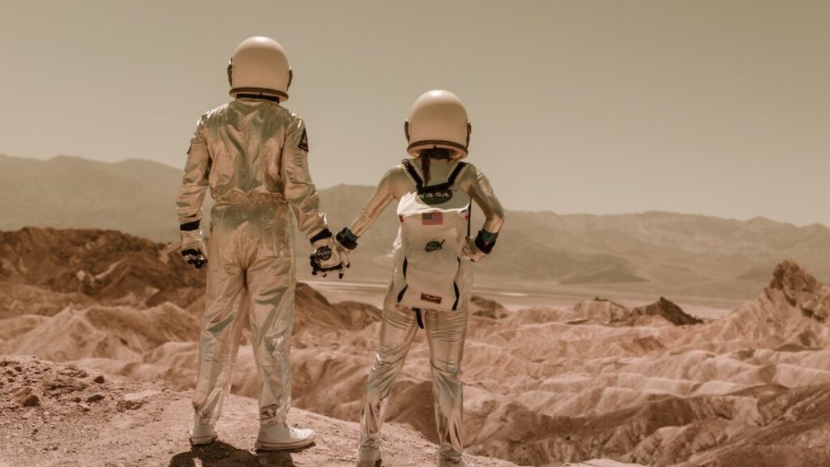 Astronauts Holding Hands Standing on Brown Mountains