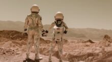 Astronauts Holding Hands Standing on Brown Mountains