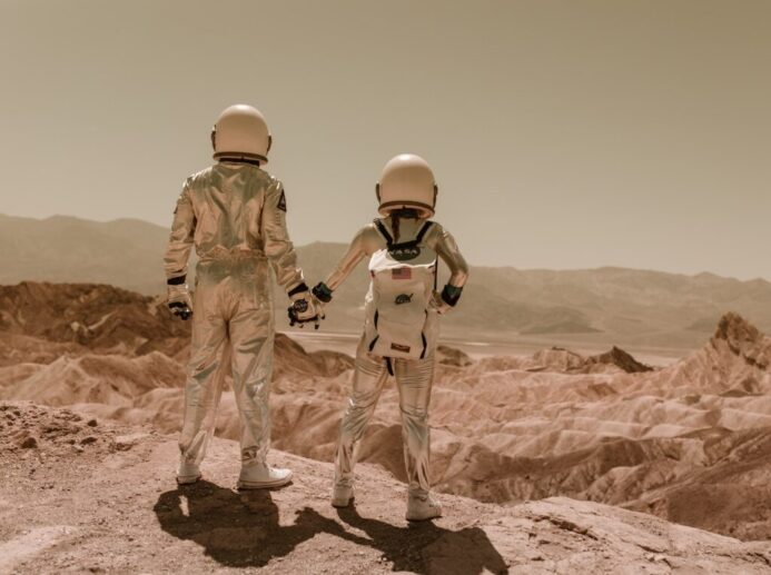 Astronauts Holding Hands Standing on Brown Mountains