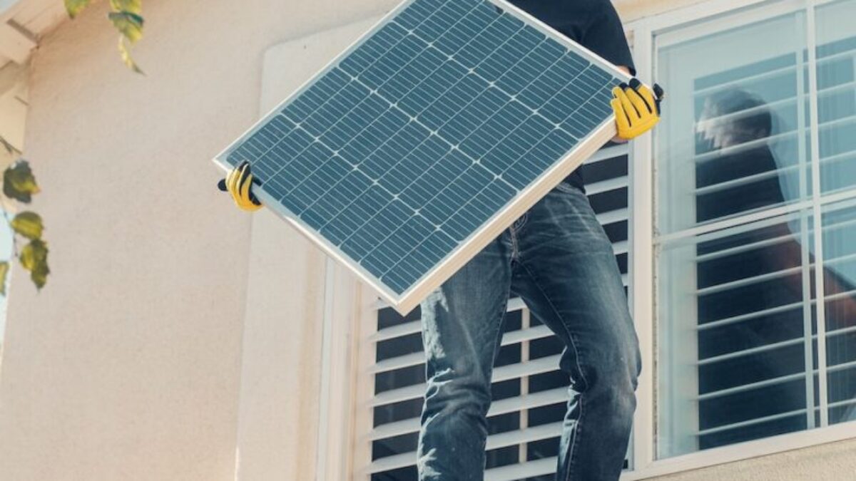 A Man in Black Shirt Standing on the Roof while Holding a Solar Panel