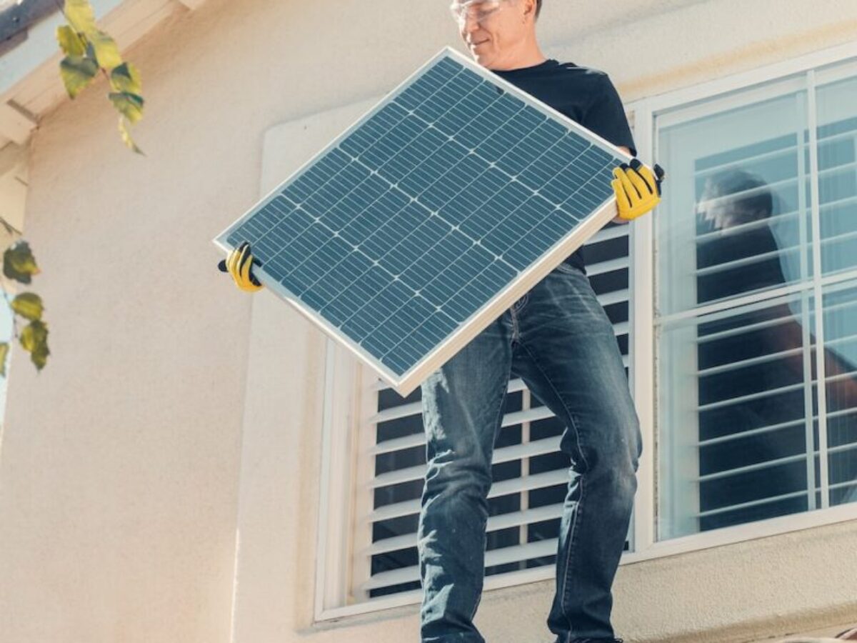 A Man in Black Shirt Standing on the Roof while Holding a Solar Panel