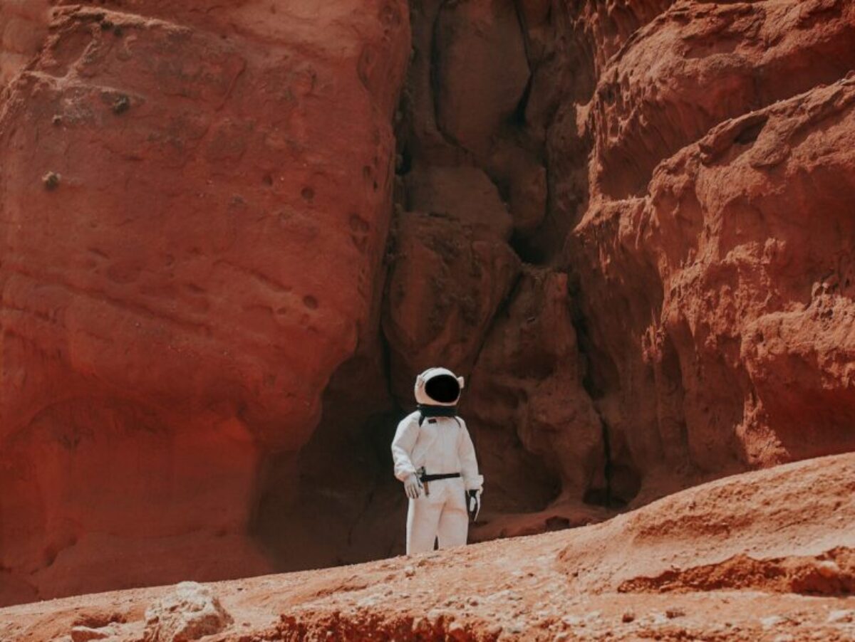 photography of astronaut standing beside rock formation during daytime