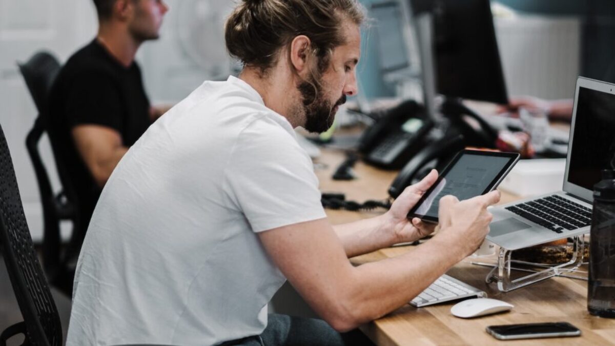 man holding turned-on iPad in front of turned-off MacBook Air
