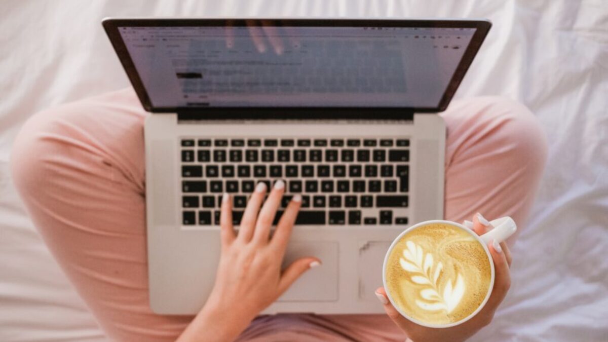 person using MacBook Pro and holding cappuccino