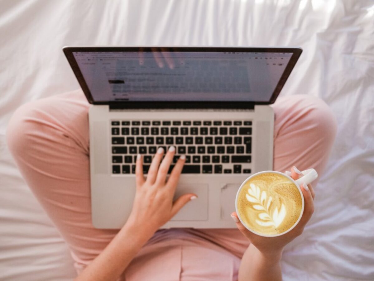 person using MacBook Pro and holding cappuccino