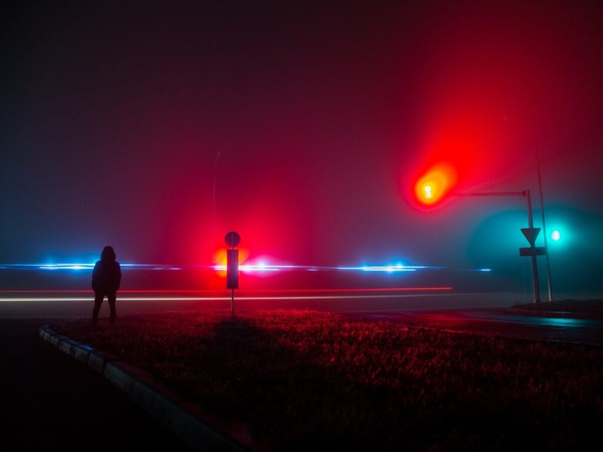 Unrecognizable Person Observing Red and Blue Lights on Road at Night