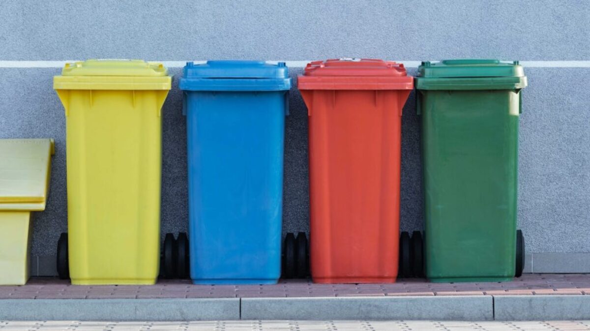 four assorted-color trash bins beside gray wall