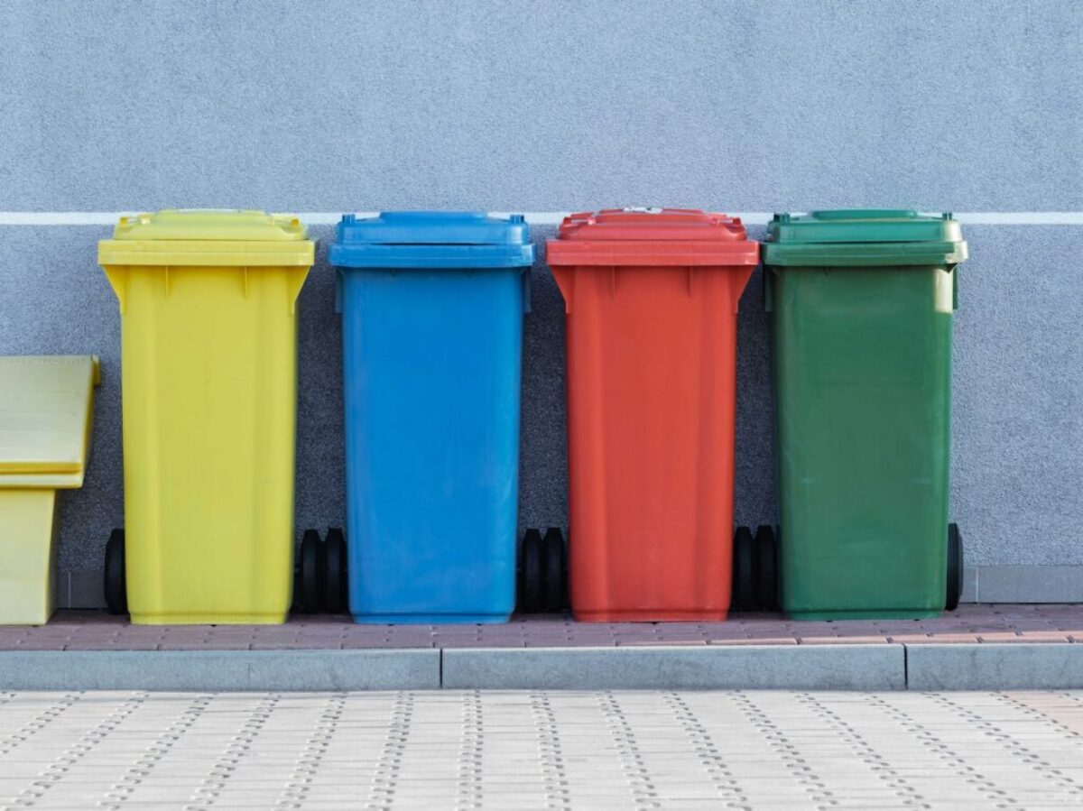 four assorted-color trash bins beside gray wall